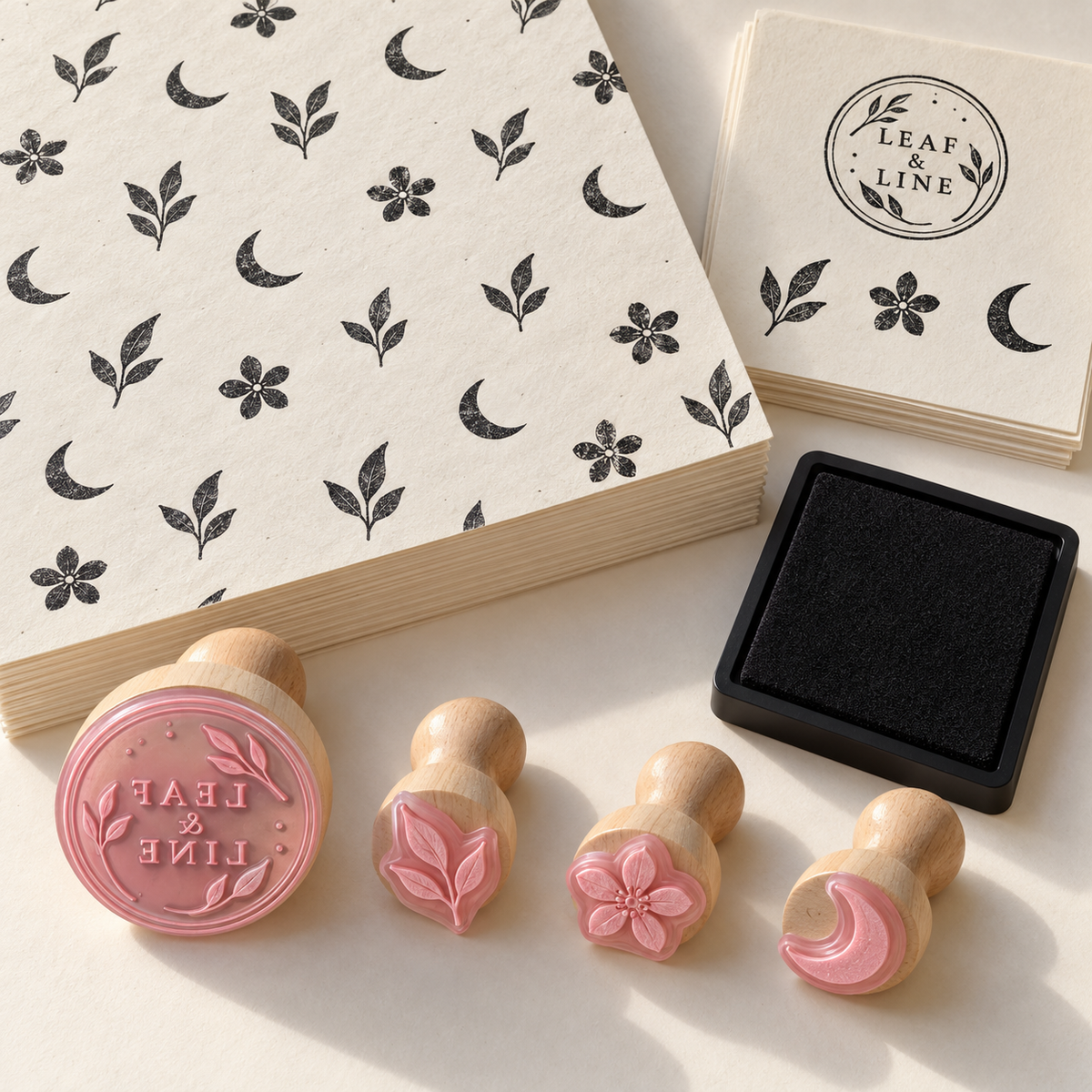 AI concept of Pattern Wrap Studio: one wood-mounted logo stamp, three pink contour-cut motif stamps, black pad, wrapping sheets and practice sheets. Fictional Leaf & Line design. Representative quantities shown; proposed kit has 50 wrapping sheets and 10 practice sheets.